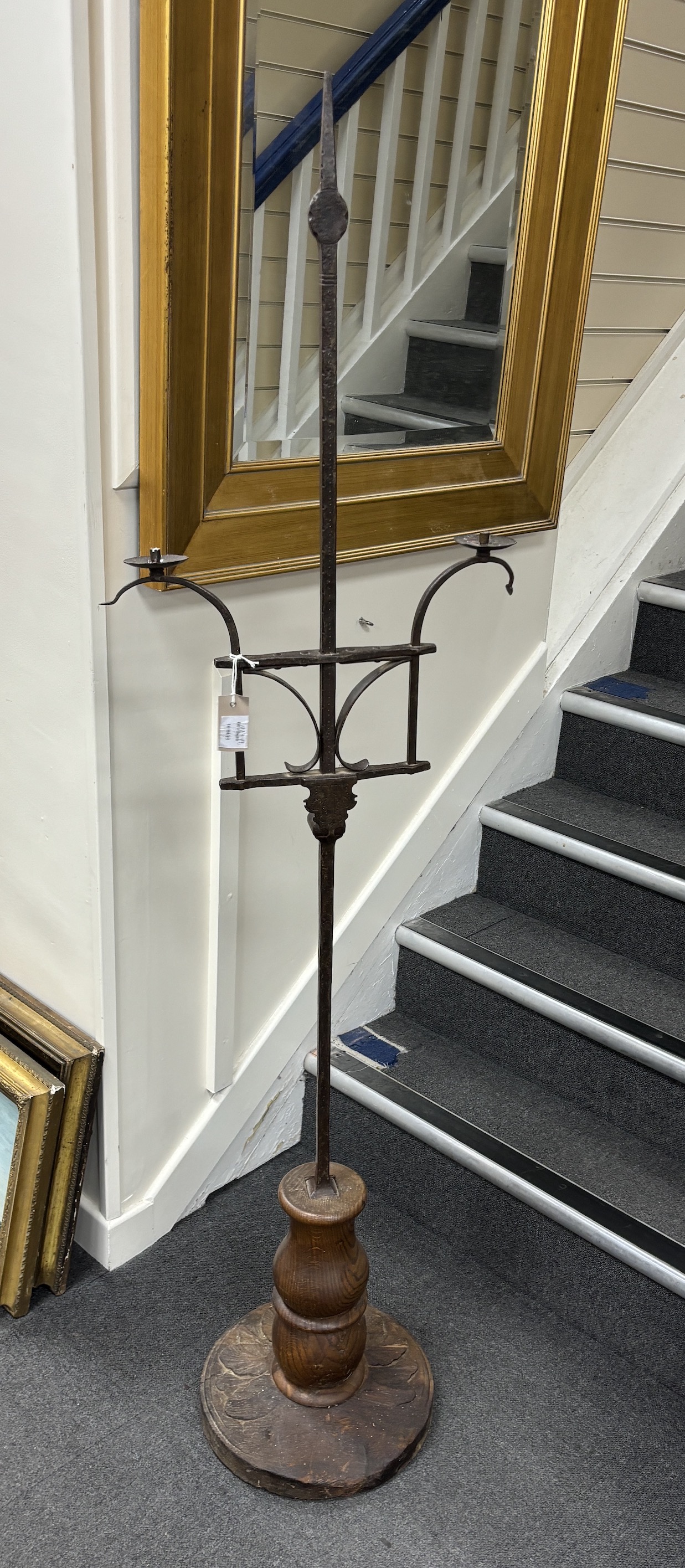A wrought iron twin branch floor standing candelabra, with oak base, height 174cm, Provenance- Brede Place, East Sussex, a former residence of the Frewen family from 1712-1936.